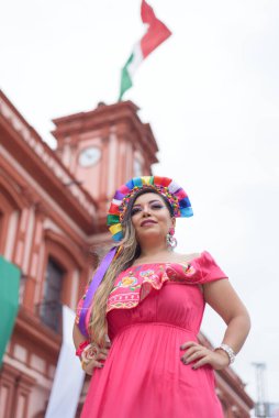 Geleneksel elbise giyen Meksikalı kadın. Sokak Meksika bayrağının renkleriyle süslenmiş. Cinco de Mayo kutlaması.