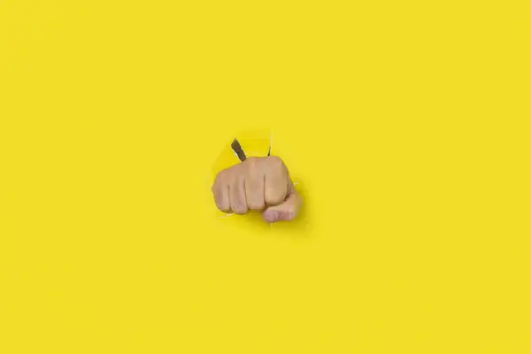 Fist punch through yellow paper background. Concept of aggression, punch, break, protest.