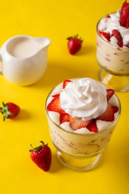 Sarı arka planda, cam bardakta kremalı çilek. Üst Manzara. Boşluğu kopyala.