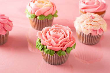 Pembe kağıtta renkli kekler. Çiçek şeklinde tereyağı kremalı süsleme.