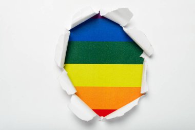 Torn hole in white paper revealing the LGTBQ flag . Rainbow flag.