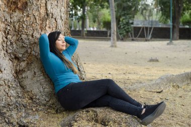 Düşünceli bir tavırla bir ağaca yaslanmış bir kadın..