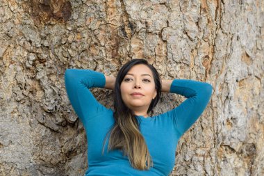 Düşünceli bir tavırla bir ağaca yaslanmış bir kadın..