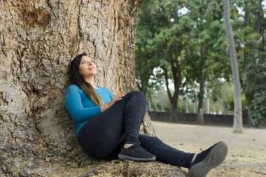 Düşünceli bir tavırla bir ağaca yaslanmış bir kadın..