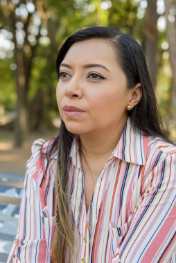 Yüzü asık bir kadın portresi, halka açık bir parkta oturuyor..