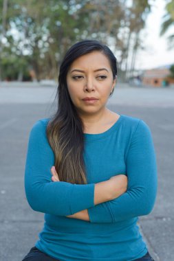 Halka açık bir parkta kollarını kavuşturmuş endişeli ve düşünceli bir şekilde oturan bir kadın..