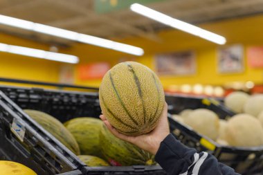 Süpermarketin rafında çizgili karpuz tutan bir kadın..