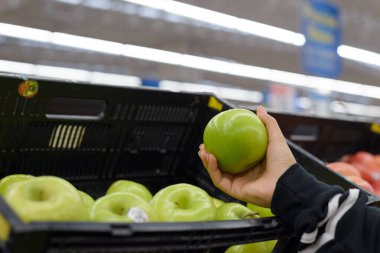Süpermarkette yeşil elma tutan bir kadın..