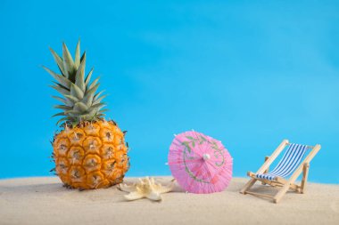 Mavi arkaplanlı deniz kumu üzerinde ananas. Yaz arkaplanı.
