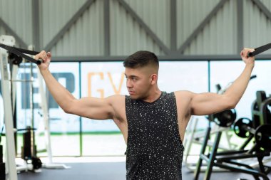 Spor salonunda kablo kullanan genç bir adam. Kollarını kaldırdı ve kabloyu aşağı çekiyor, kaslarını çalıştırıyor..