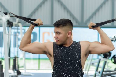 Spor salonunda kablo kullanan genç bir adam. Kollarını kaldırdı ve kabloyu aşağı çekiyor, kaslarını çalıştırıyor..