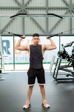 Spor salonunda kablo kullanan genç bir adam. Kollarını kaldırdı ve kabloyu aşağı çekiyor, kaslarını çalıştırıyor..