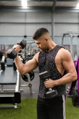 Spor salonunda ağırlık kaldıran bir adam pazularına bakıyor..