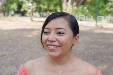 Saçları topuz gibi arkadan çekilen genç bir kadın pembe omuzlu, parlak bir şekilde gülümsüyor..