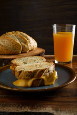Ahşap bir masanın arkasında bir bardak meyve suyu ve ekmek ile ızgara peynirli sandviç. Boşluğu kopyala.