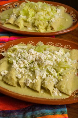Kil tabakta servis edilen marul ve peynirli yeşil enchilada. Renkli masa örtüsü. Kapat.