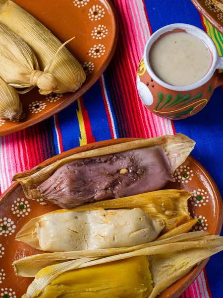 Çamurlu bir tabakta farklı aromalı tamaleler ve renkli bir serapta bir fincan atole. Tatlı tamale..