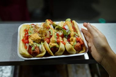 Soğan, domates ve soslar da dahil olmak üzere çeşitli malzemelerle dolu birkaç sosisliye yakın çekim.