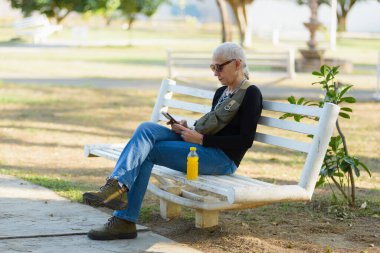 Parktaki bankta oturan orta yaşlı lezbiyen kadın cep telefonunu kontrol ediyor..