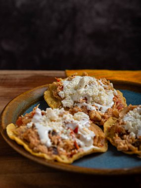 Tavuk tinga soslu Tostadas, ahşap bir masada peynir ve krema. Tipik Meksika yemekleri..