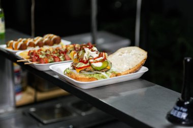 Close-up of a freshly prepared burger, garnished with various toppings, resting on a disposable white tray.