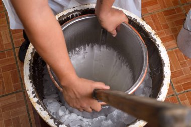 Erkek eller, daha büyük buz dolu bir kap içinde metal bir dondurma kabını dikkatle çevirir..