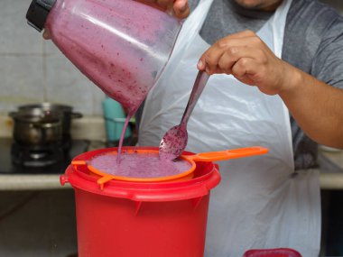 Bir insan canlı mor bir meyve suyunu dikkatlice süzgeçten geçirip kırmızı bir konteynıra koyar..