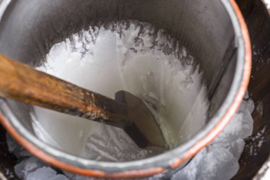 Metal bir çalkantı içinde, buzdan bir yatakta çırpınan, kremalı, beyaz dondurmayı çalkalayan ahşap küreğin yakın çekimi..