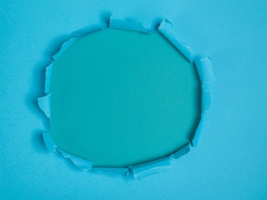 Açık mavi kağıtta yırtılmış dairesel bir delik, deniz mavisi arkaplanı ortaya çıkarıyor..