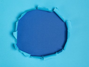 Açık mavi kağıtta yırtılan dairesel bir delik zıt bir koyu mavi arkaplanı ortaya çıkarır.