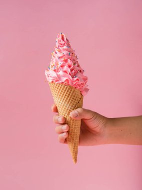 Bir el, bol bol renkli serpiştirilmiş canlı pembe dondurmayla dolu uzun bir waffle külahını tutar..