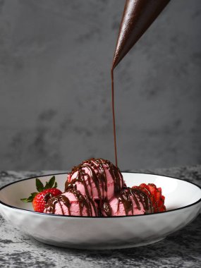 Üç kepçe çilekli dondurma, taze çilek ve zengin çikolata yağmuruyla süslenmiş..