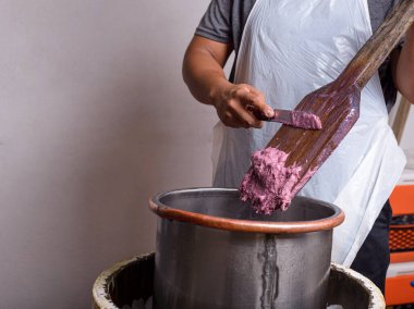 Önlük takan biri, ahşap bir kürek kullanarak metal bir kaba bir kepçe canlı mor dondurma karışımı ekler..