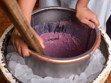Elleri buzla çevrili metal bir kasede mor dondurmayı döndürür. Geleneksel yöntem gösterildi; rustik ayar.