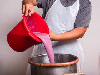 Plastik önlüklü biri kırmızı kovadan büyük paslanmaz çelik karıştırma tankına canlı mor dut püresi döker.