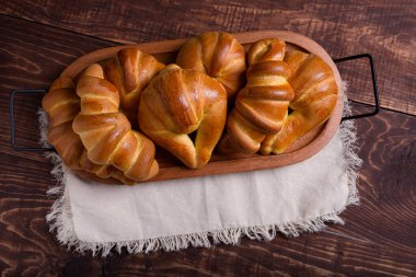 Ahşap tepside taze pişmiş ekmek ruloları ve kruvasanlardan oluşan bir karışım bulunur..