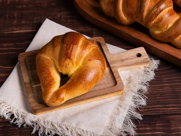 Yeni pişmiş bir kruvasan, çarşaf bezine yerleştirilmiş, ahşap bir tahtanın üzerinde duruyor..