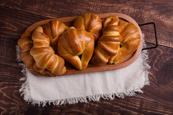 Ahşap tepside taze pişmiş ekmek ruloları ve kruvasanlardan oluşan bir karışım bulunur..