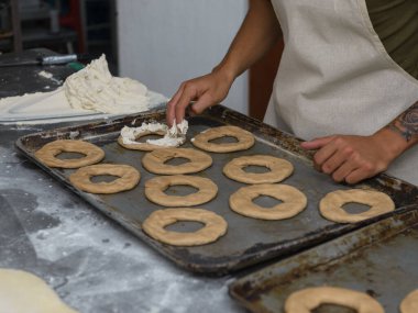 Bir fırıncı titizlikle halka şeklindeki hamur parçalarını kremalı bir tepsiyle doldurur..