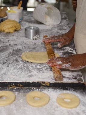 Erkek eller ustalıkla hamuru un kaplı bir yüzeyde yuvarlar, donut halkaları için hazırlar..
