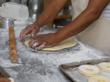Erkek eller ustalıkla hamuru un kaplı bir yüzeyde yuvarlar, donut halkaları için hazırlar..