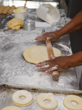 Erkek eller ustalıkla hamuru un kaplı bir yüzeyde yuvarlar, donut halkaları için hazırlar..