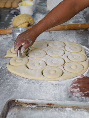 Kapalı bir yüzey üzerinde donut hamurunu şekillendirmek için ustalıkla bir kesiciyi kullanarak, kızartma için hazırlanan eller..