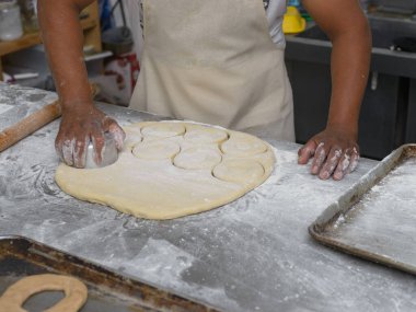 Kapalı bir yüzey üzerinde donut hamurunu şekillendirmek için ustalıkla bir kesiciyi kullanarak, kızartma için hazırlanan eller..