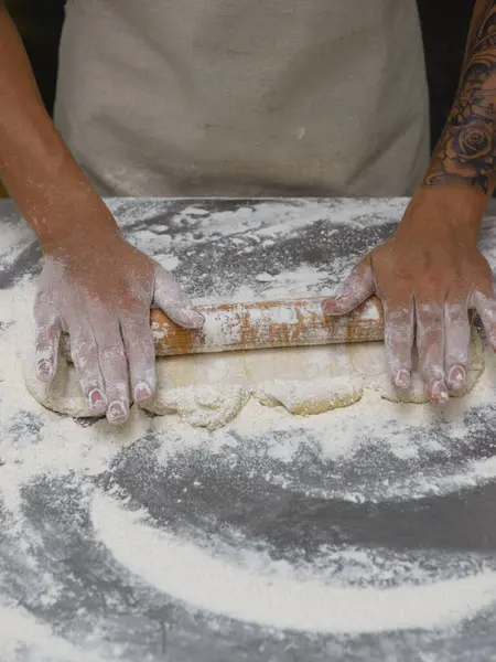 Ustalıkla hamuru yuvarlarken, un kaplı bir yüzeye ahşap bir oklamayla yakın plan çekiyoruz..