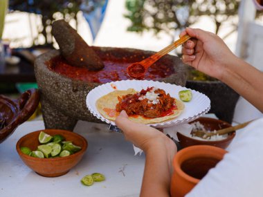 Bir el, kağıt tabakta lezzetli görünen bir takoya baharatlı kırmızı sos ekler..