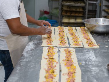 Bir fırıncı uzun hamur şeritlerine jambon, peynir ve jalapeno karışımını dikkatlice yayar..