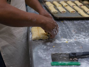 Bir fırıncının elleri, un kaplı bir yüzeydeki susam tohumlu hamur işlerini dikkatlice şekillendirir..