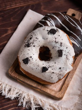İki lezzetli çörek, biri çikolatalı, diğeri kremalı kurabiye, ahşap bir tahtanın üzerinde, fırfırlı keten peçetenin üzerinde dinleniyor..