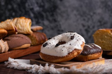 İki lezzetli çörek, biri çikolatalı, diğeri de tahta bir tahtanın üzerinde kremalı kurabiye. Pişmiş yiyeceklerle bulanık arkaplan.